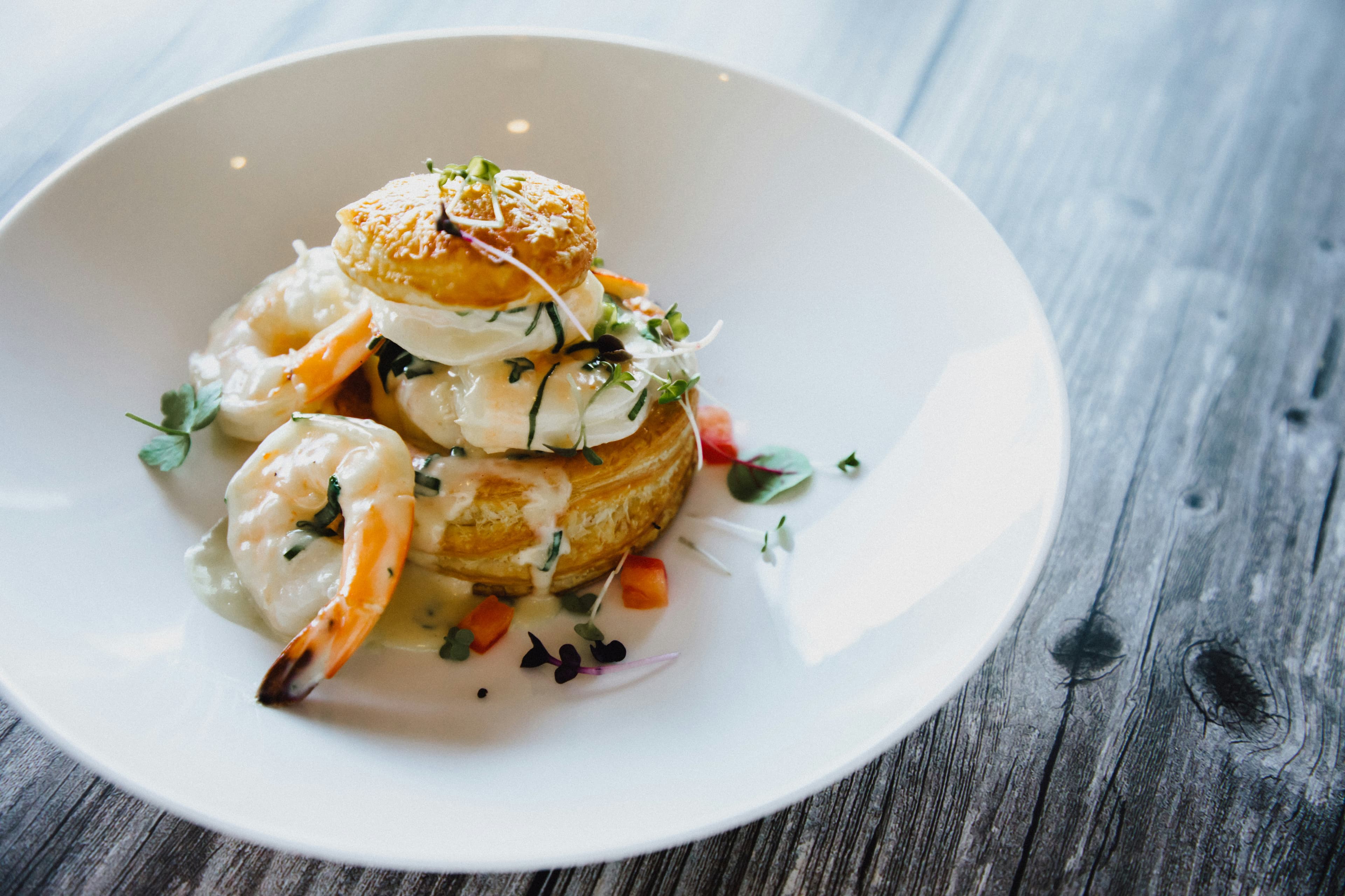 A bowl of shrimp topped with a biscuit, creamy sauce, and garnished with herbs.