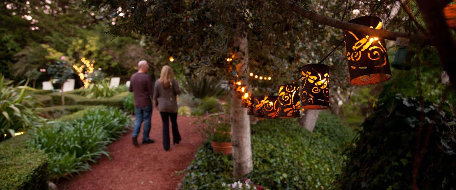 A couple strolls down a garden path illuminated by decorative lanterns.