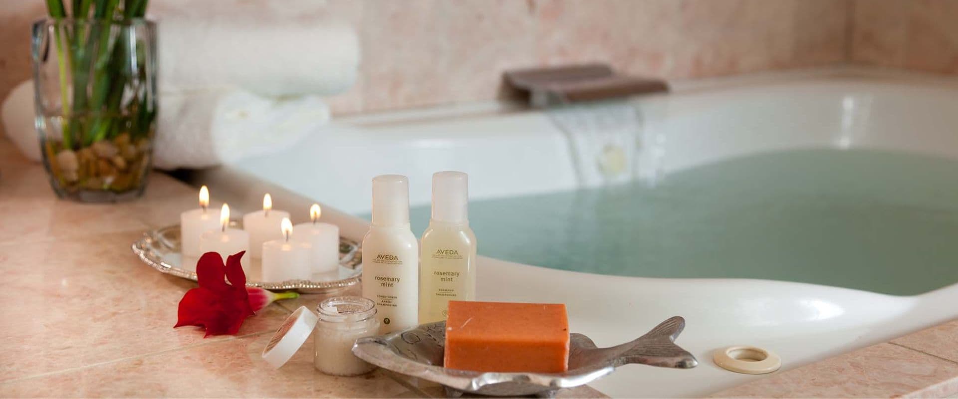 A relaxing spa setting featuring a bathtub, candles, bath products, a bar of soap, and fresh towels.