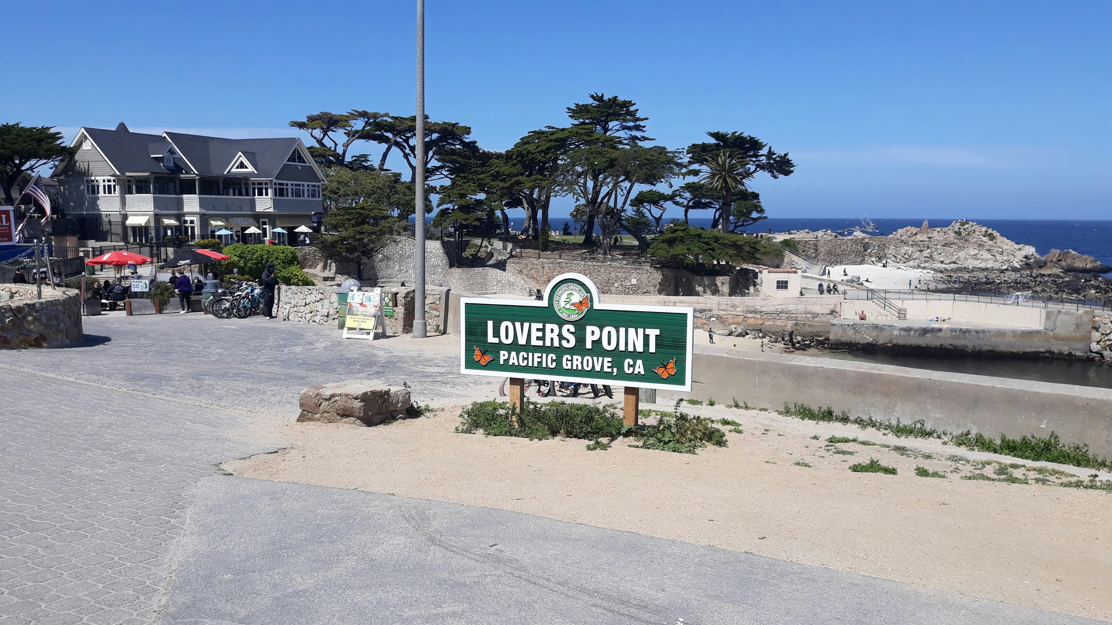 Sign for Lovers Point in Pacific Grove, CA, with ocean and scenery in the background.