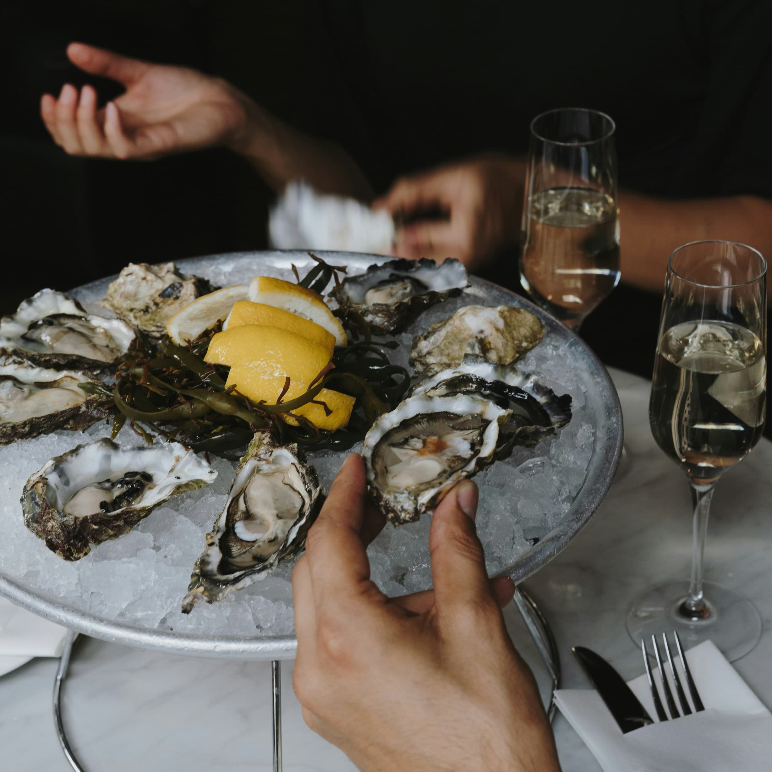 A plate of oysters on ice garnished with lemon slices, accompanied by two glasses of champagne.