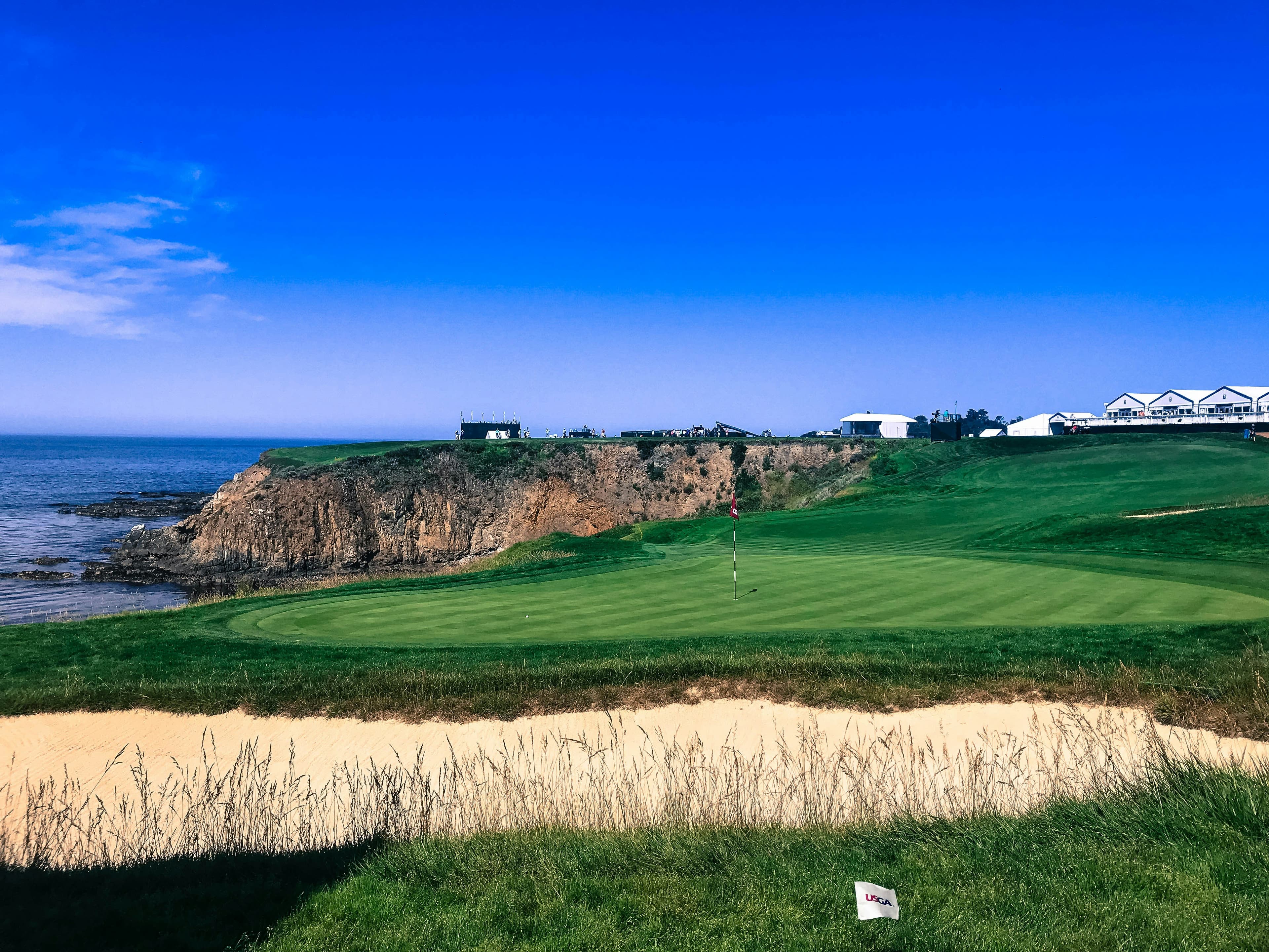 A scenic golf course overlooking the ocean with a clear blue sky.