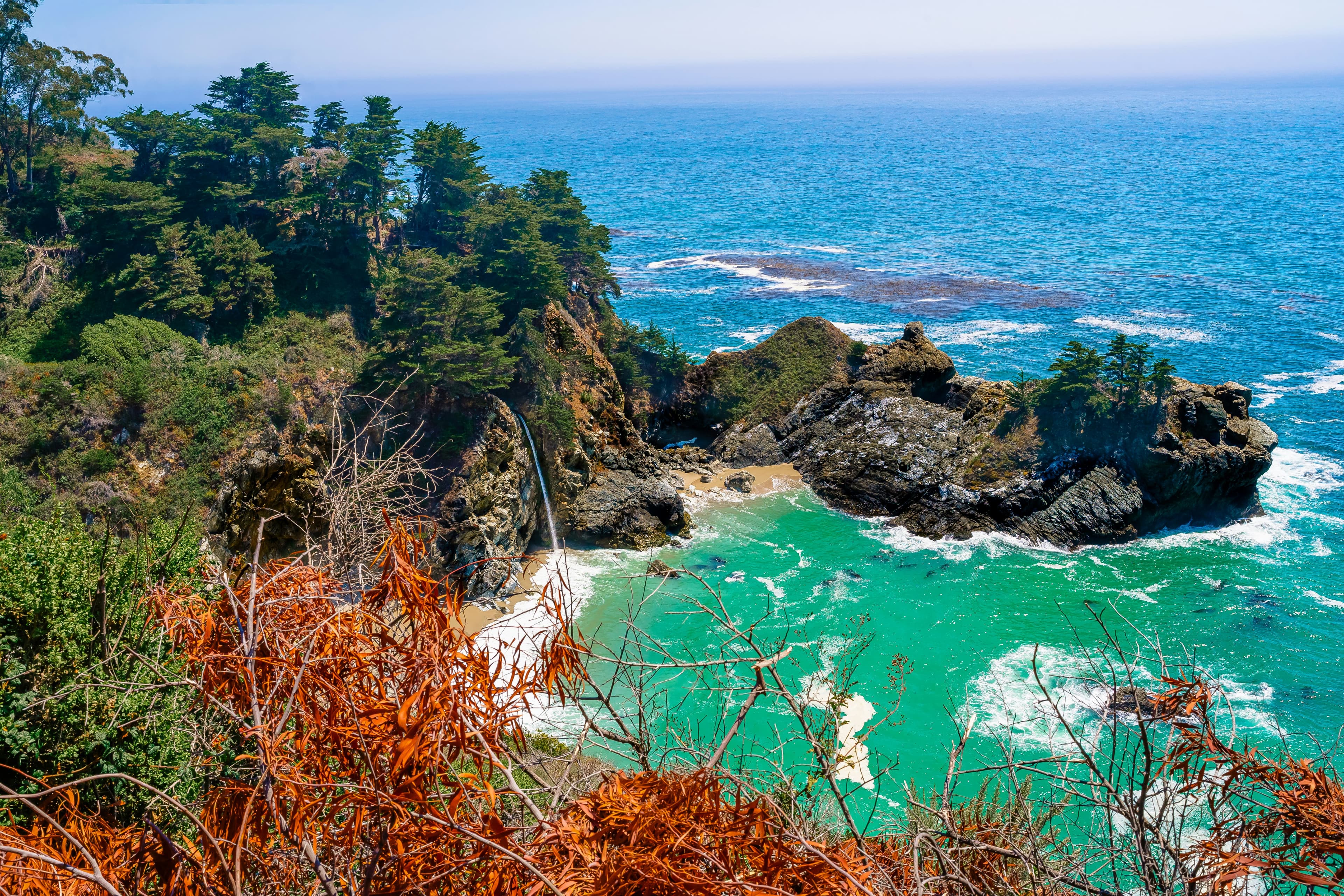 A scenic coastal view featuring turquoise waters, rocky outcrops, and lush greenery.