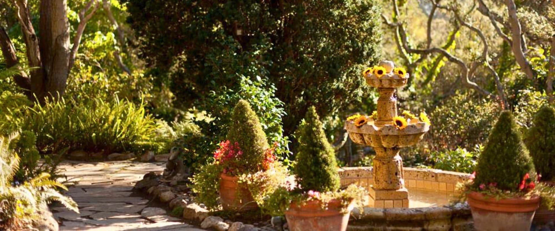 A serene garden path winding past a fountain adorned with sunflowers.