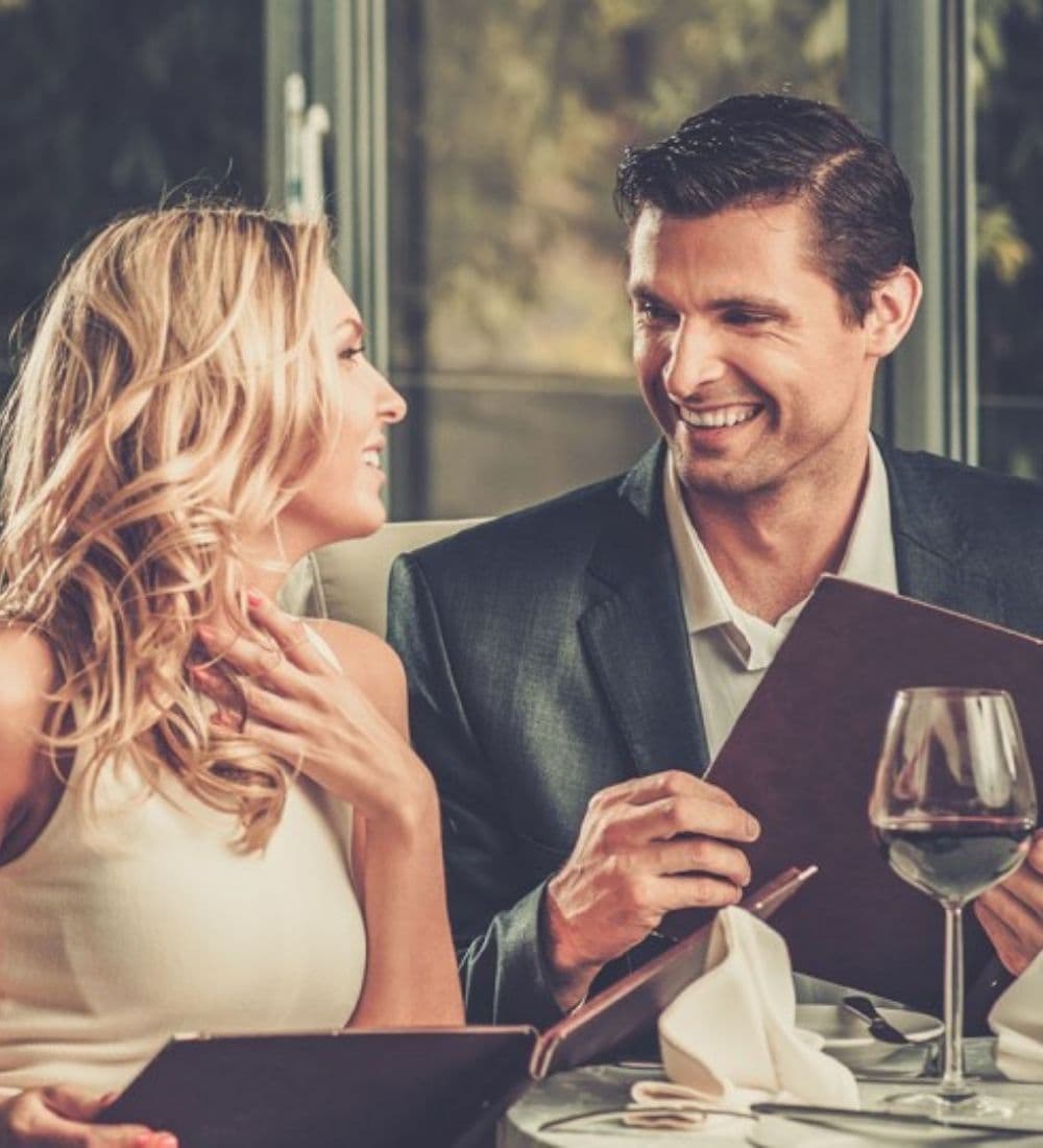 A smiling couple enjoys a meal together while browsing the menu in an elegant setting.