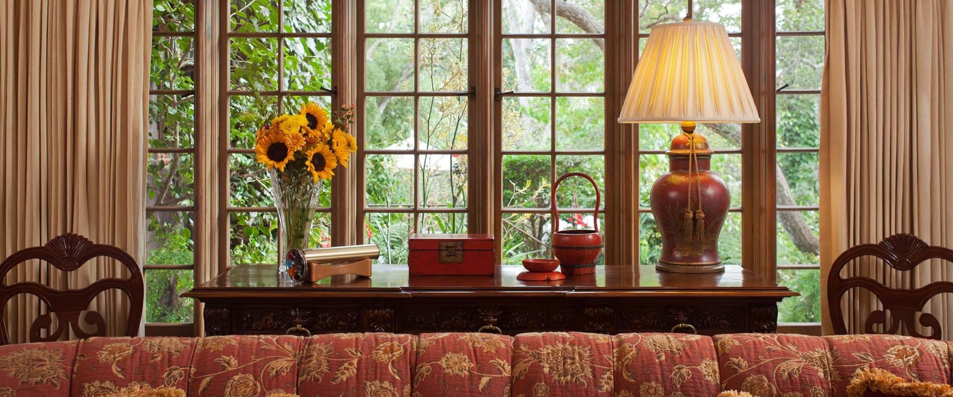 Sofa table with lamp, vase of flowers next to a large window and plush tufted couch Sofa table with lamp, vase of flowers next to a large window and plush tufted couch