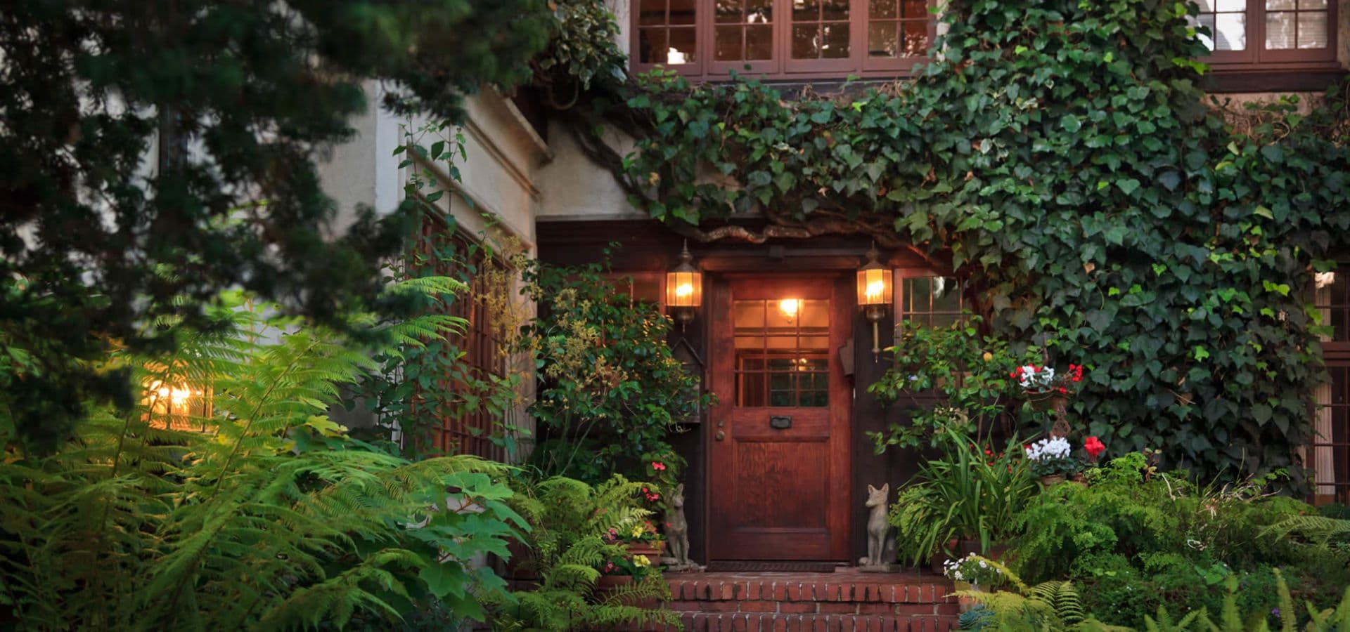 Wooden front door surrounded by lush greenery and blooming flowers.